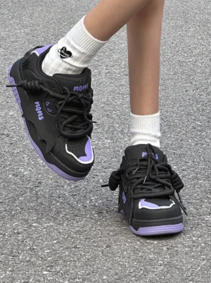 Black and purple chunky platform skate sneakers worn with white crew socks in an on-foot streetwear scene, showing the graphic side profile and exaggerated thick laces