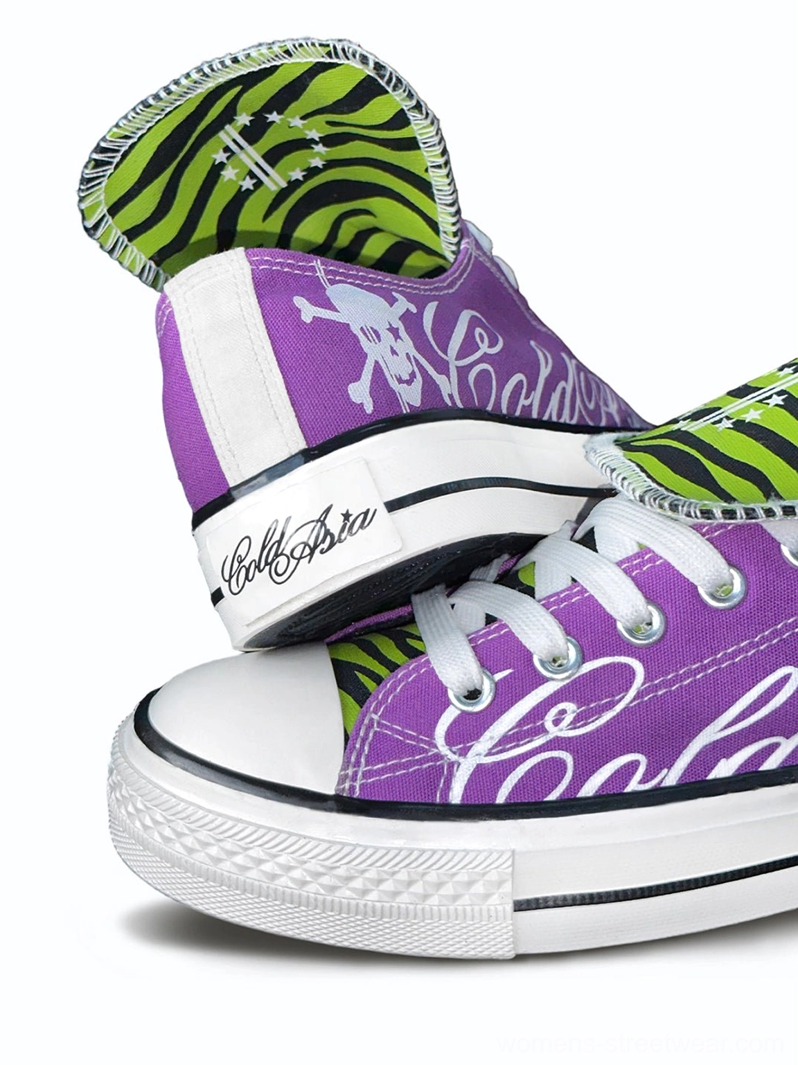 Close angled view of purple canvas streetwear sneakers showing white script graphics, rubber midsole detailing, skull heel artwork, and zebra print tongues