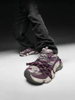 Purple chunky retro sneakers shown from a low angle with layered lacing and a neutral grey color-blocked upper styled with dark denim