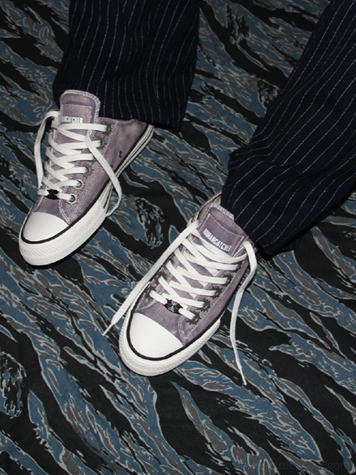 Pair of purple distressed low-top skate sneakers styled with dark pinstripe trousers on a blue graphic fabric background
