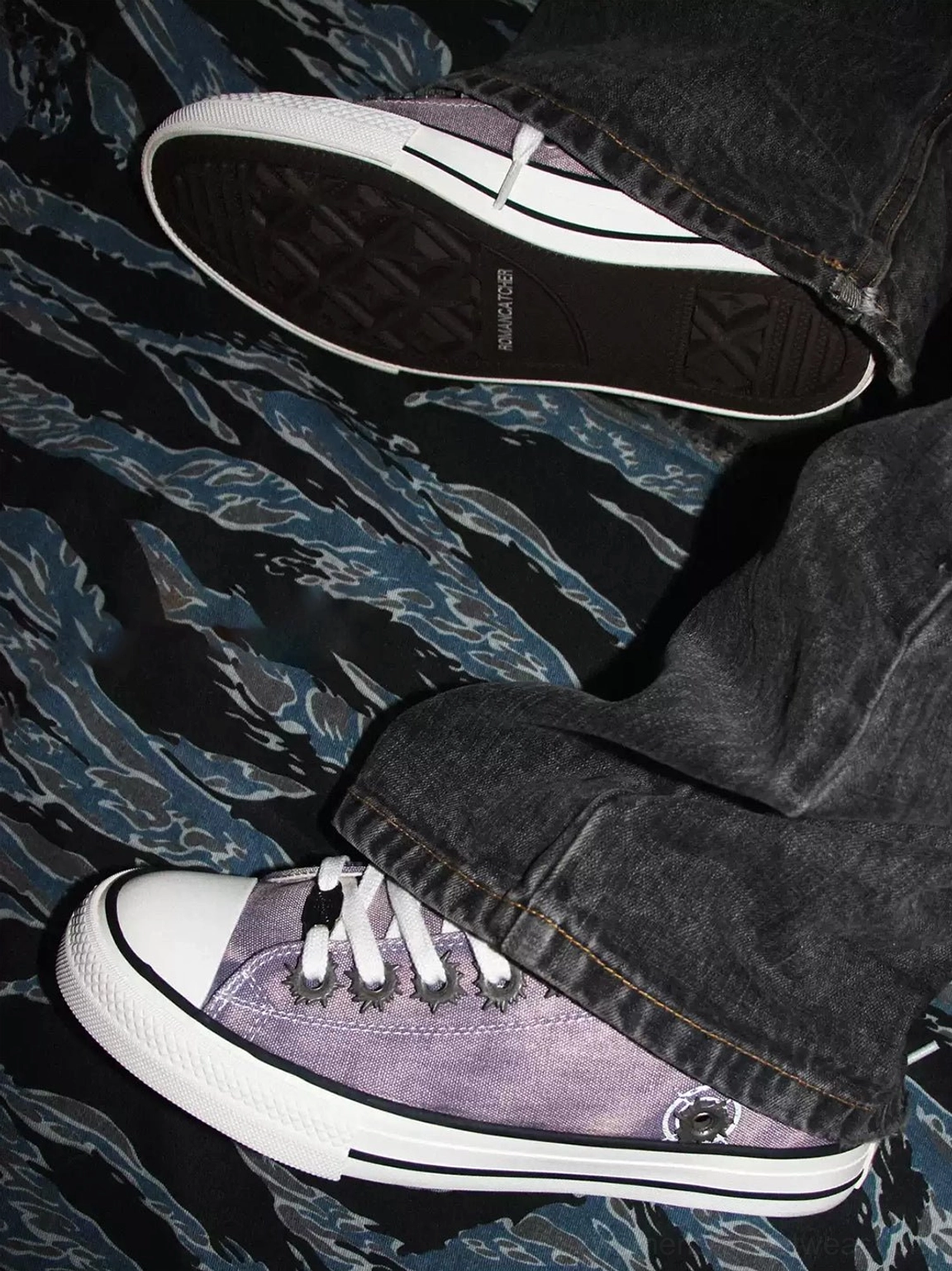 Purple distressed skate sneaker worn with dark grey washed denim showing white laces patterned rubber outsole and casual streetwear details