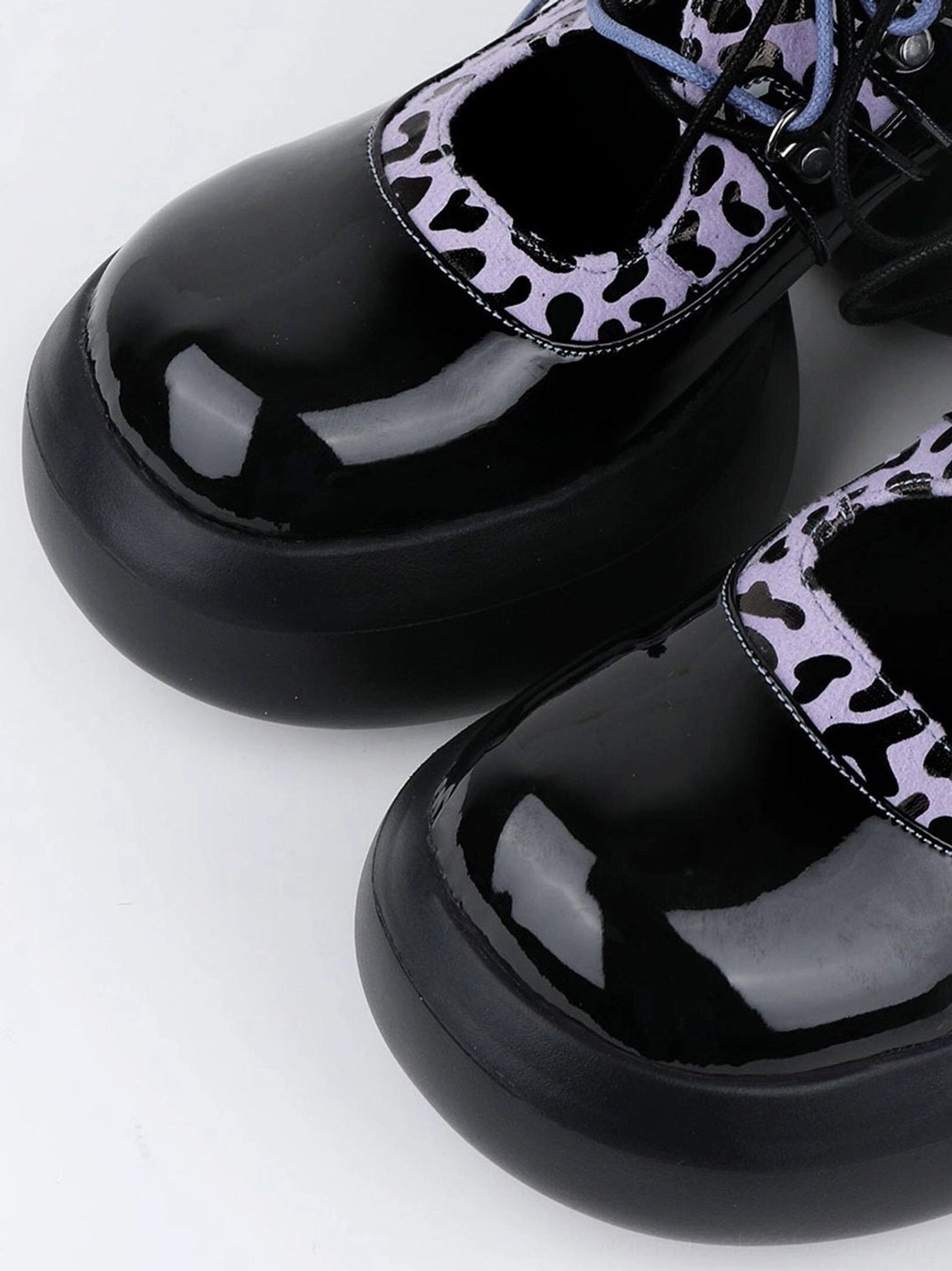 Top view close-up of glossy black patent toe caps, purple leopard panels, and blue-purple laces on platform Oxford shoes