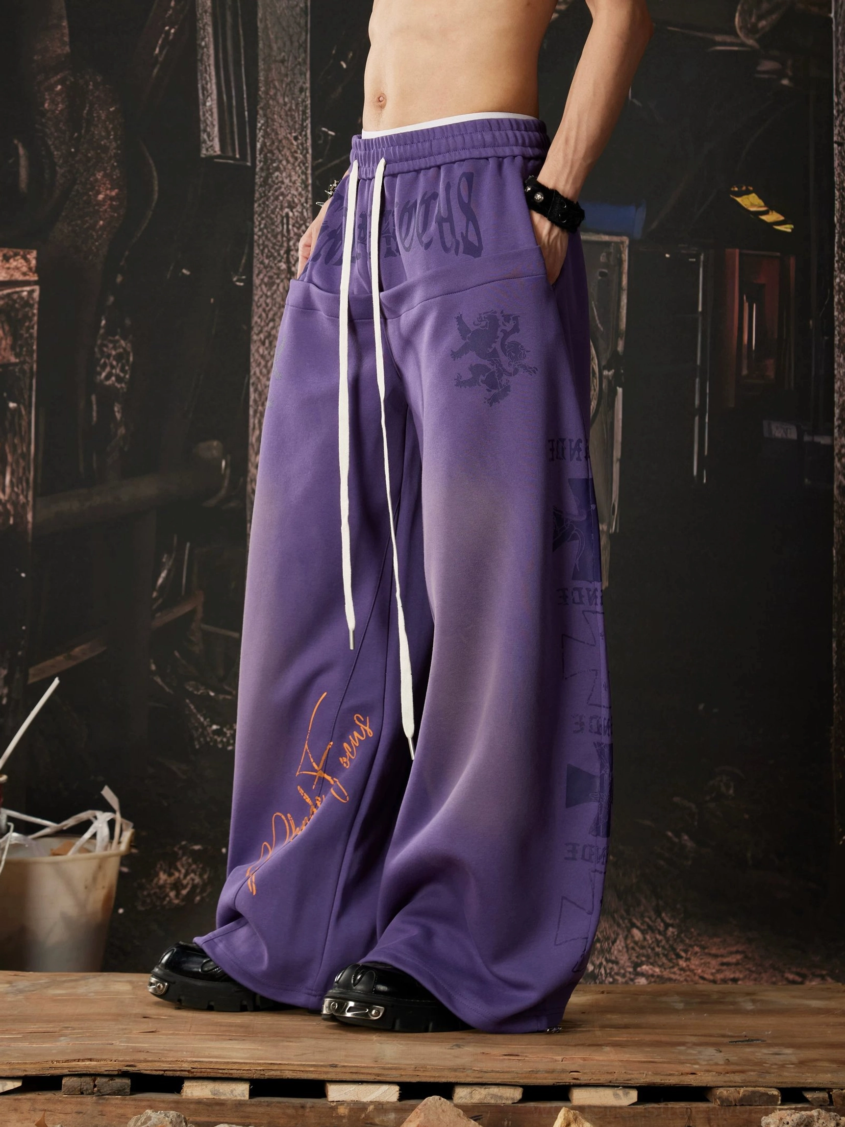 Purple wide leg streetwear pants with heraldic lion crest print, handwritten signature graffiti, gradient finish, and ultra-relaxed Y2K silhouette