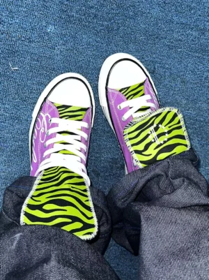 Top down view of purple zebra tongue canvas sneakers worn with dark denim jeans, white laces, rubber toe caps, and low streetwear soles