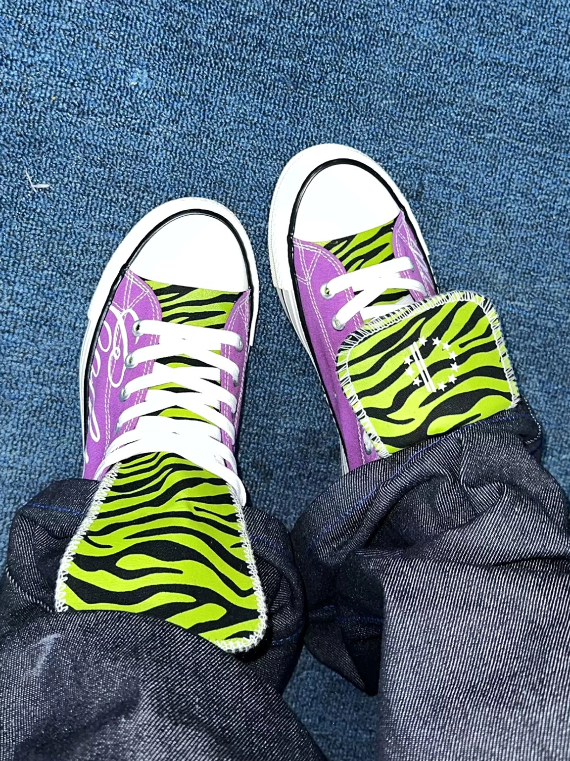 Top down view of purple zebra tongue canvas sneakers worn with dark denim jeans, white laces, rubber toe caps, and low streetwear soles