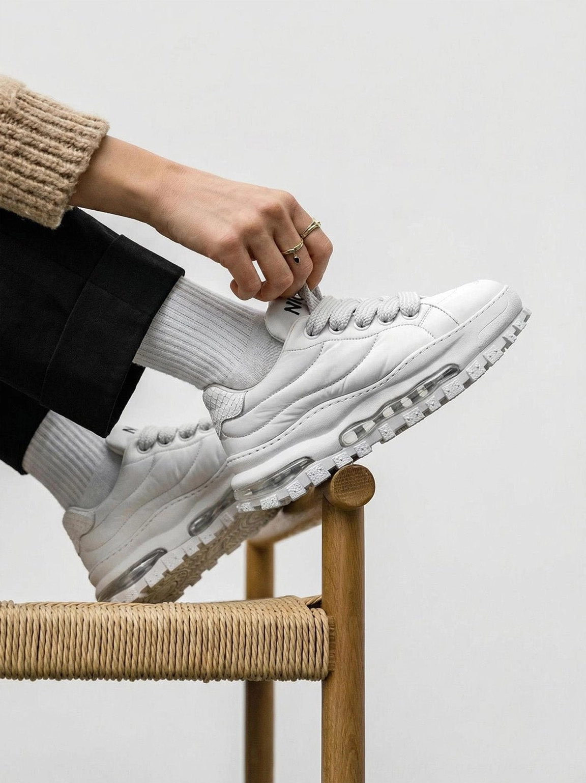 White leather trail runner sneakers with chunky ripple tread sole worn with black trousers and white socks