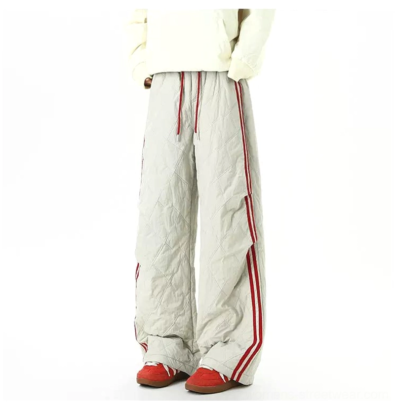 Back view of light gray quilted wide-leg track pants with red side stripes and stacked hem over red sneakers