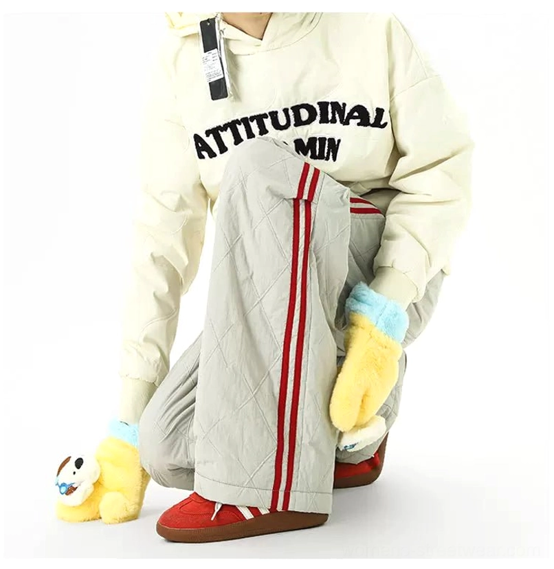 Close view of gray diamond quilted wide-leg track pants with bold red side stripes and relaxed streetwear fit