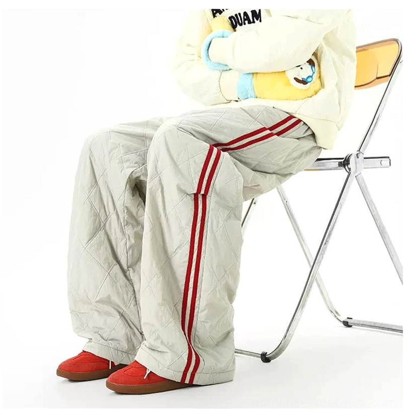 Side view of light gray padded quilted streetwear track pants with red contrast stripes in a relaxed seated outfit
