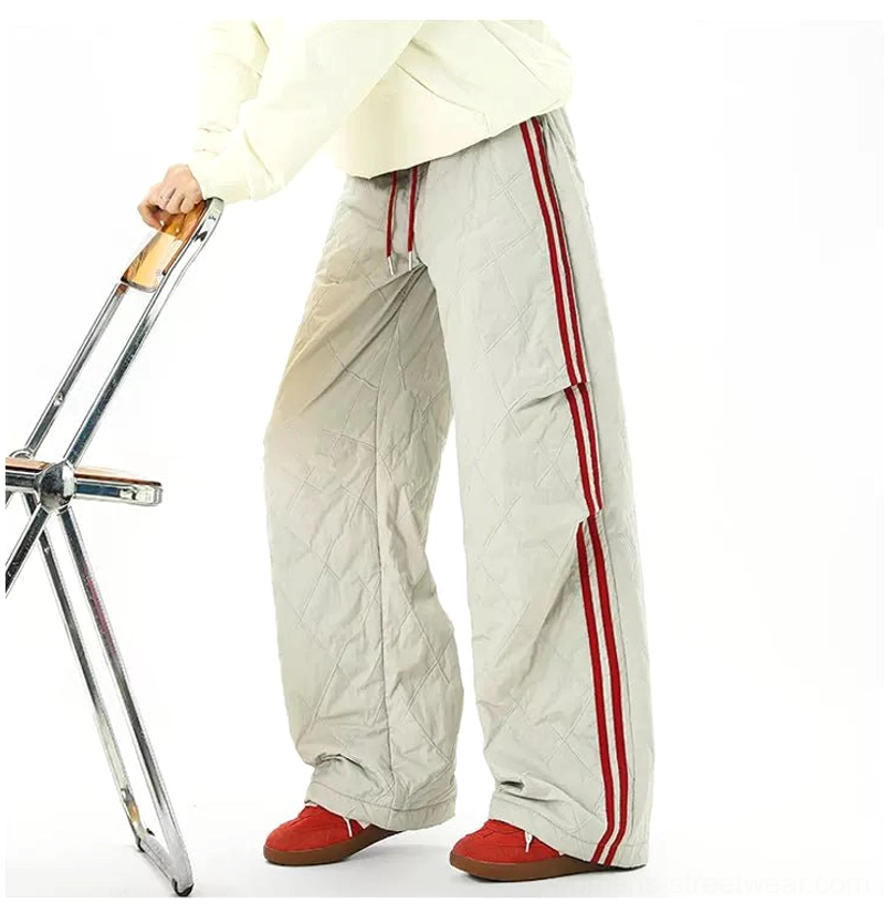 Light gray quilted streetwear pants with red contrast side stripes and long wide legs draping over sneakers