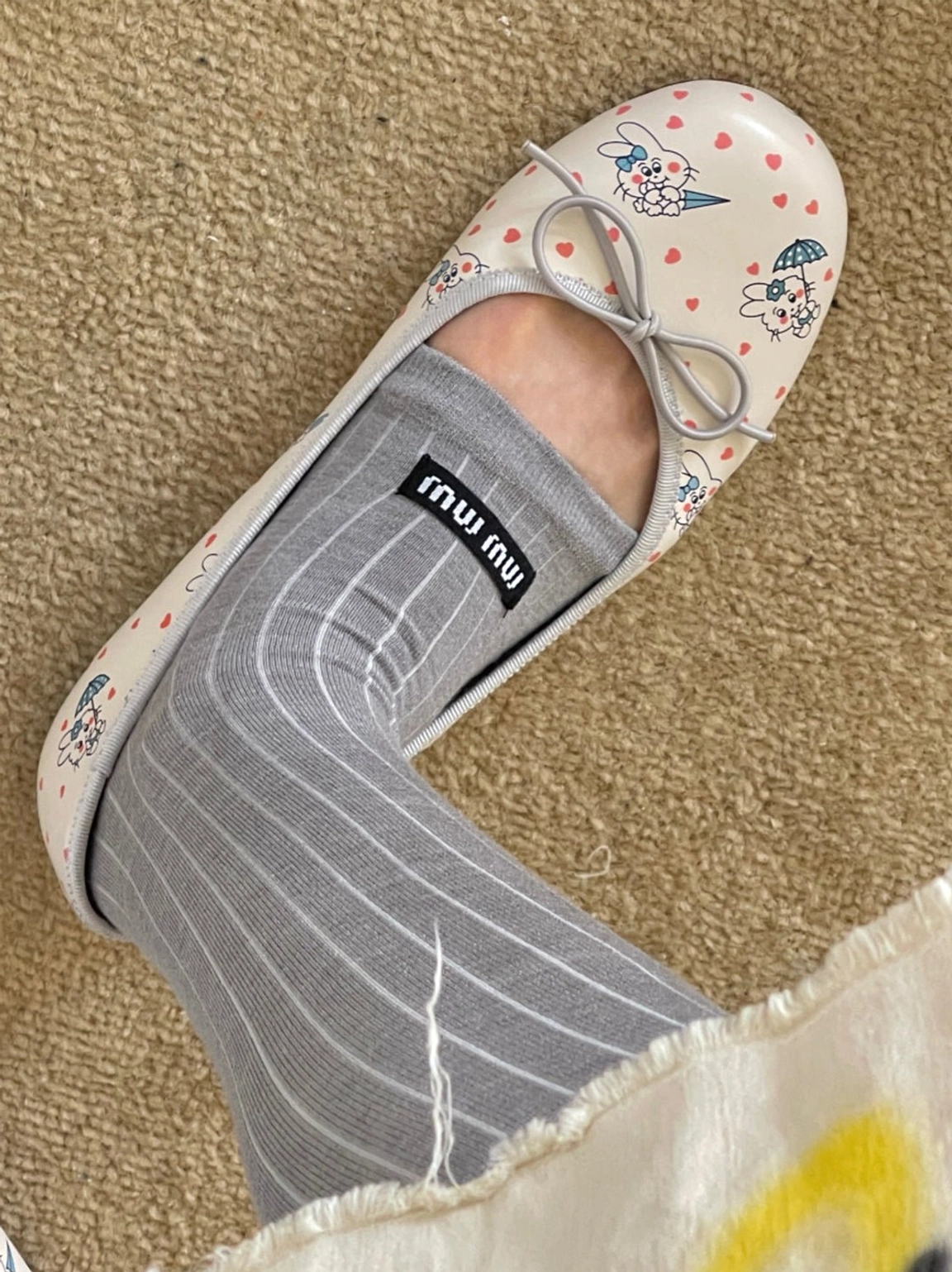Close-up streetwear styling of rabbit and heart printed square-toe ballet flats worn with ribbed gray socks and a frayed skirt