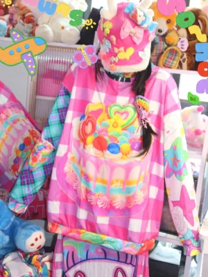 Front close up of oversized rainbow cake gingham sweater with colorful dessert graphic and mismatched printed sleeves in pink check pattern