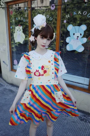Front full body view of rainbow stripe bear kawaii overall dress with white Peter Pan collar, cartoon telephone graphic, patch pockets and ruffled skirt hem