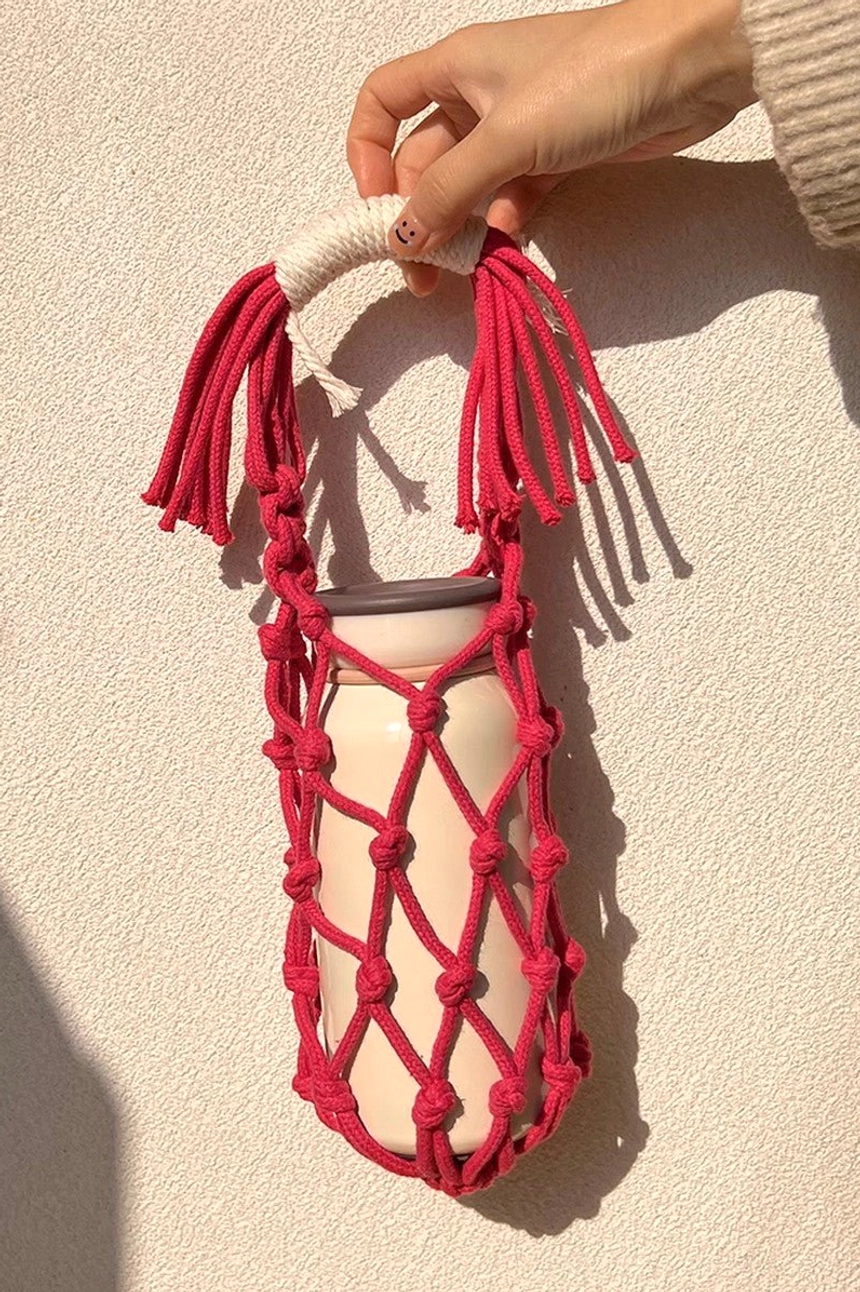 Raspberry red macrame water bottle carrier with white tumbler, featuring a hand-knotted cotton net and wrapped tassel handle