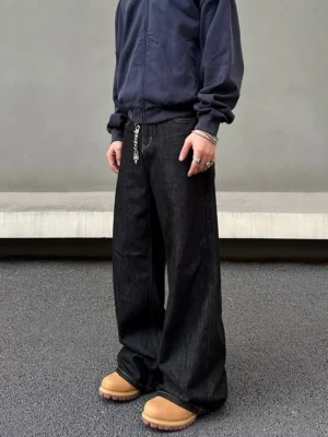 Three-quarter side view of wide-leg raw denim jeans showing the relaxed hip and thigh fit, deep indigo wash, waist chain, and chunky streetwear boots