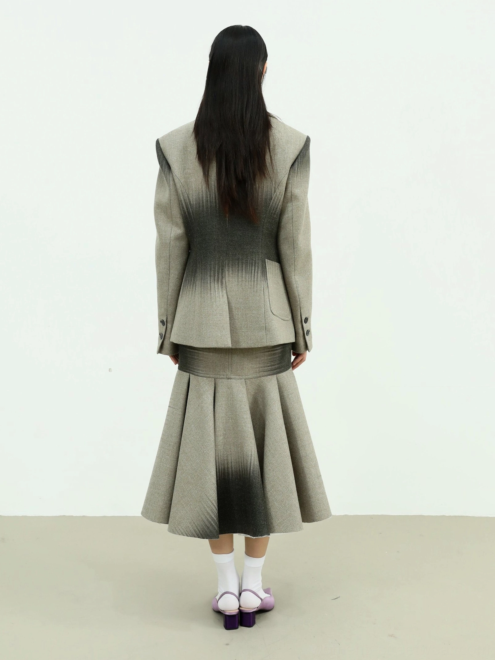 Rear view of a gray gradient fishtail maxi skirt with pleated flared hem and tailored blazer styling in Korean fashion