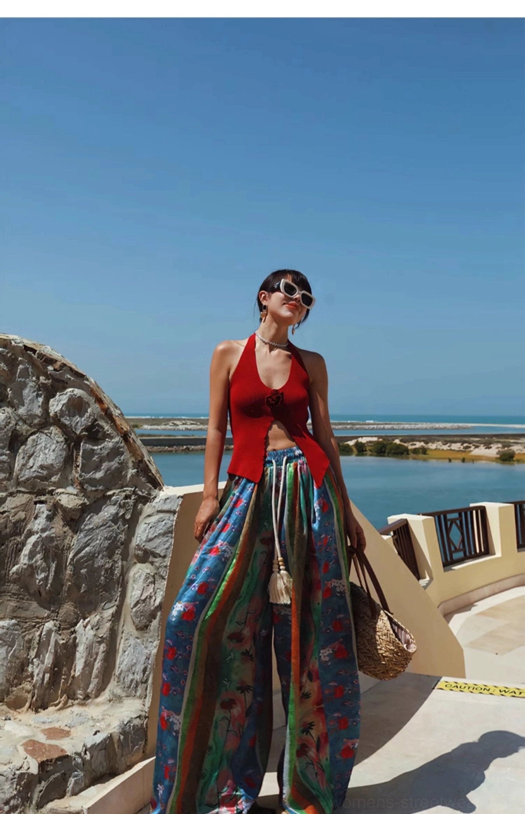 Red 3D rose halter knit top in a coastal vacation streetwear outfit with flowy printed trousers and woven bag