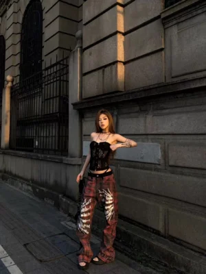 Front three quarter view of red black plaid gothic flare streetwear pants with white sigil lettering and wing graphics on a female model