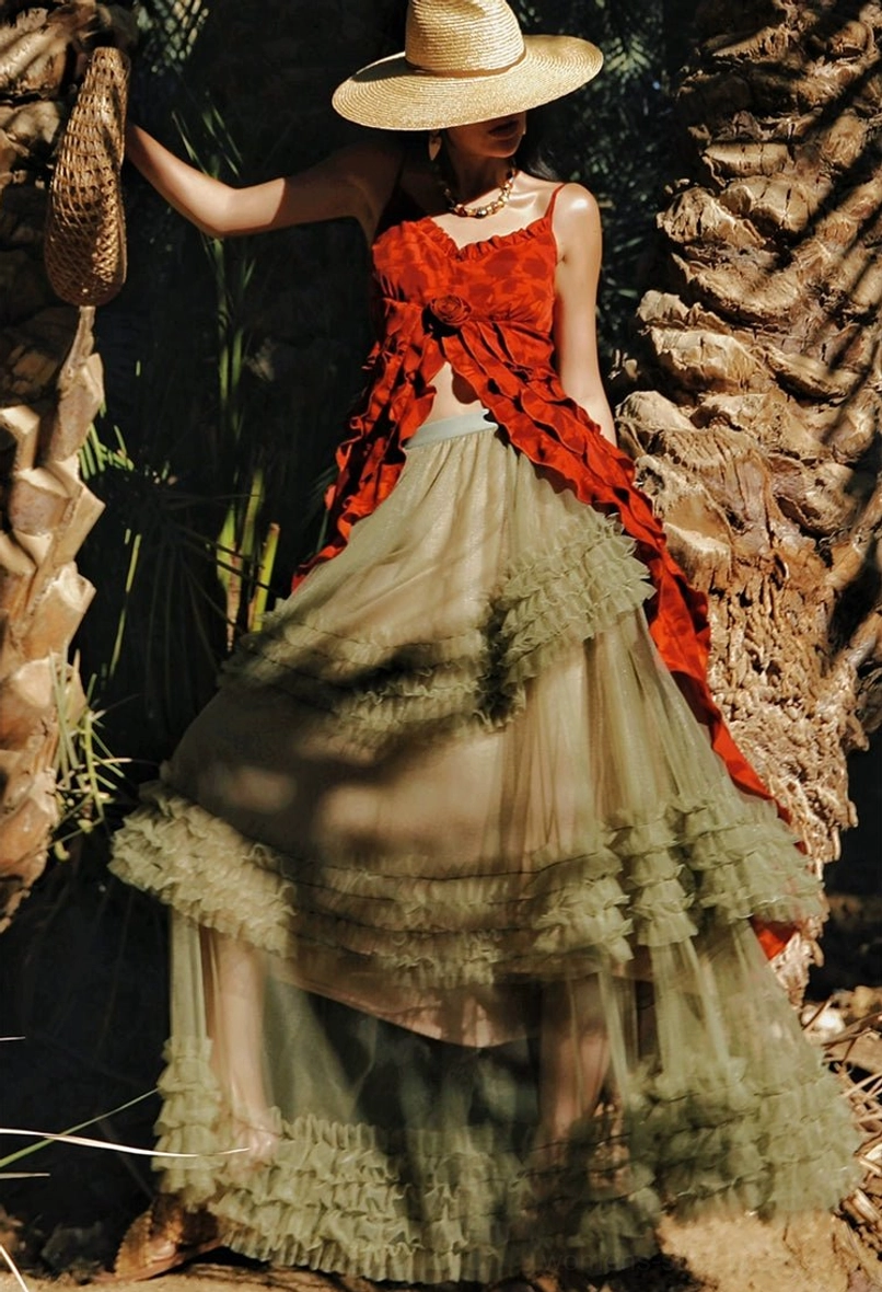 Red boho ruffle camisole top with asymmetric front hem styled with an olive green tulle maxi skirt and straw hat in a tropical garden