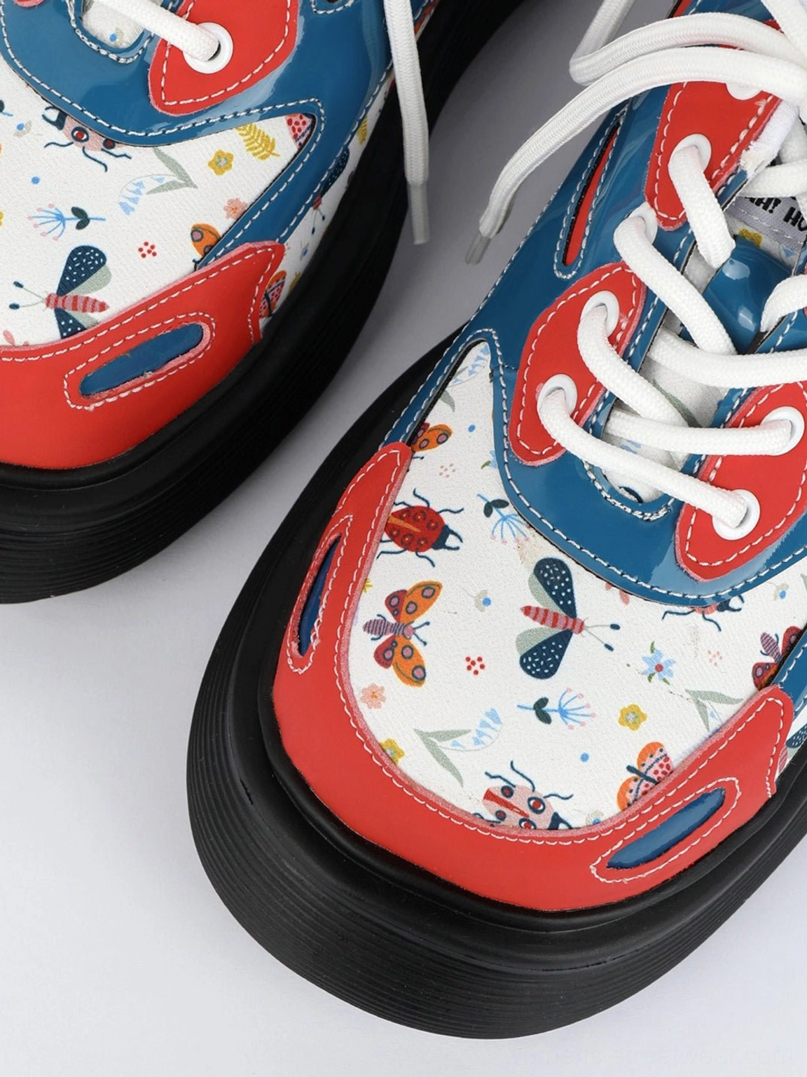 Extreme close-up of red butterfly platform derby shoe with printed panel, white eyelets, and red trim