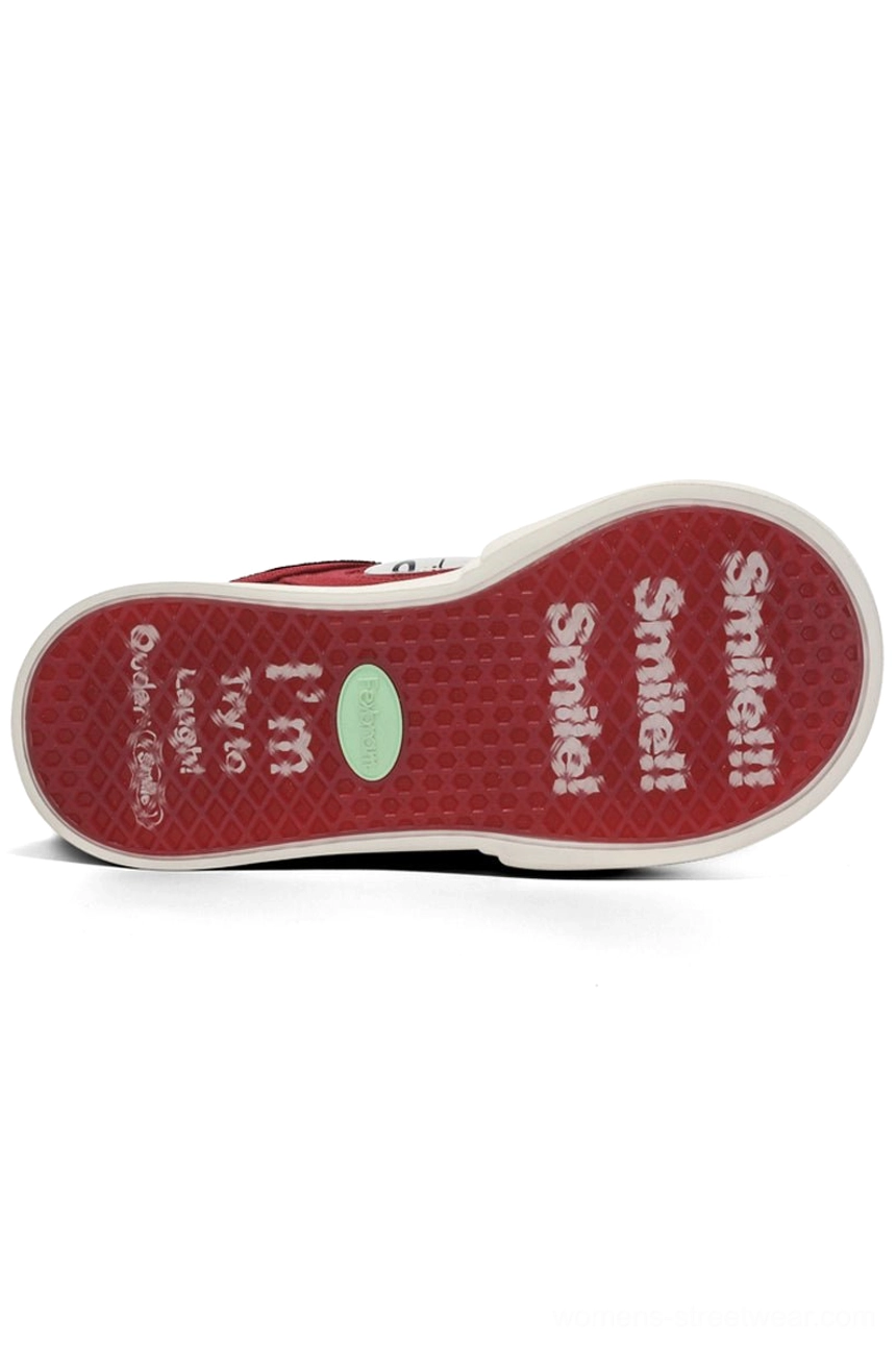Flat overhead view of red anti-slip sneaker outsole with textured grip pattern, smile-themed printed messages, and green center insole cushion patch