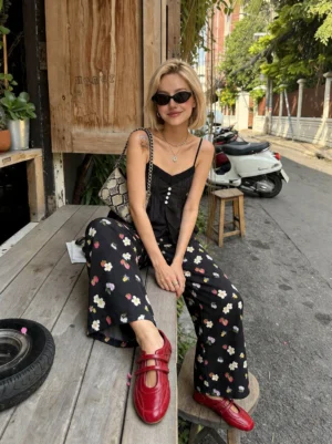 Woman wearing red crisscross strap flats with black camisole and floral wide-leg pants at an outdoor cafe