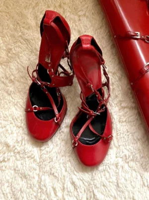 Red cross-strap round-toe high heel pumps with silver-tone buckles and adjustable crisscross straps shown from a top-down view on a soft beige carpet