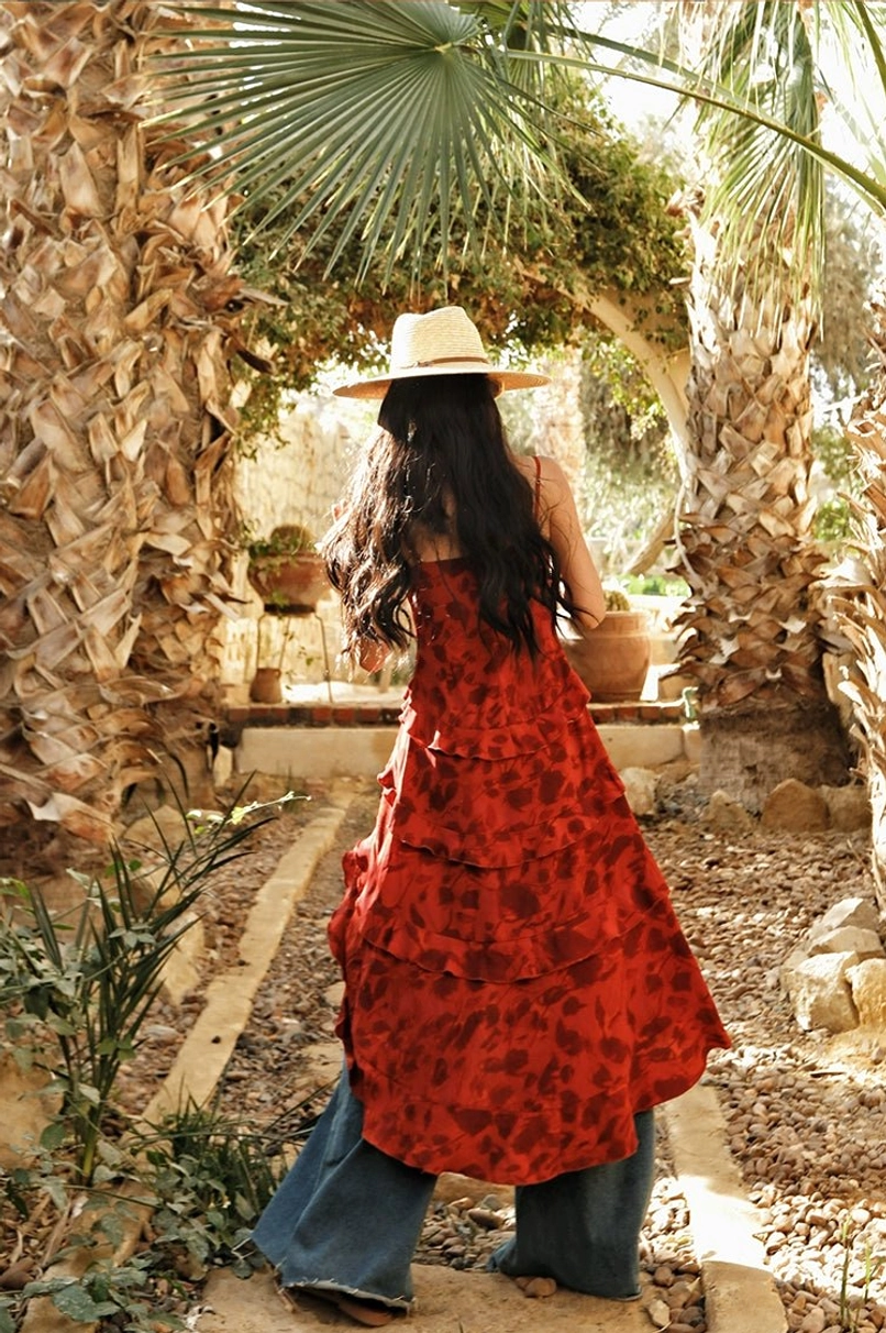 Red floral boho camisole top shown from the rear with tiered ruffled high-low hem and open spaghetti strap back in a Mediterranean stone courtyard