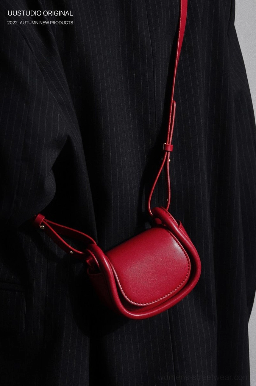Red mini saddle crossbody bag worn crossbody over a black striped tailored jacket