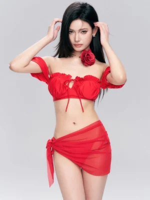 Front view of red off-shoulder ruffle bikini set with adjustable tie top, matching bottoms, sheer wrap sarong, and rose-inspired styling accessory