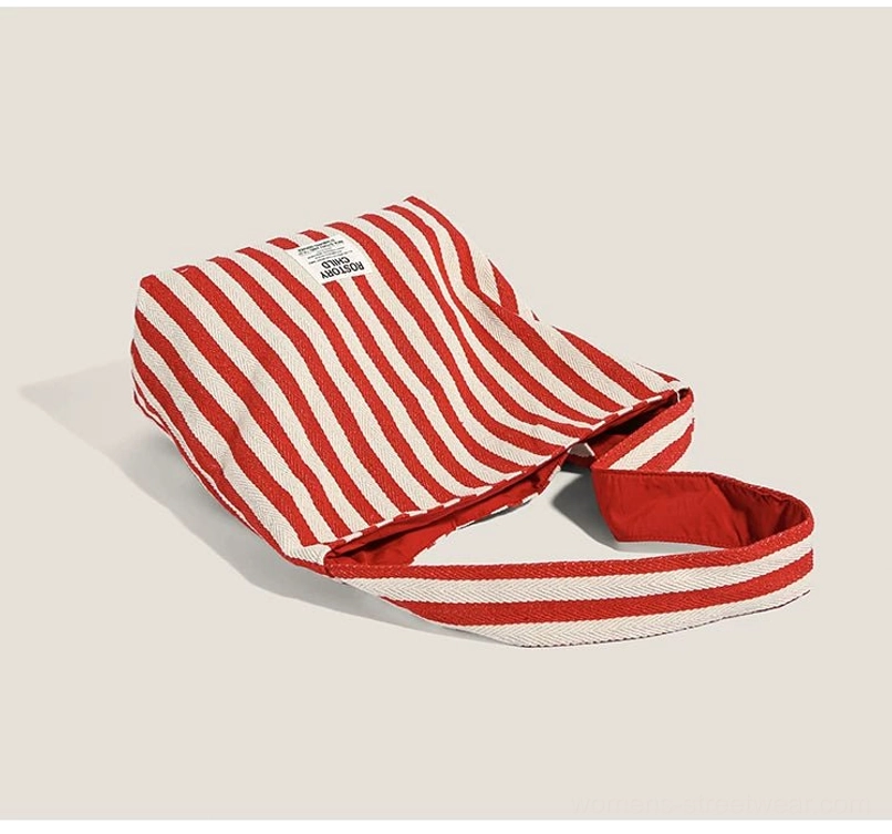 Oblique side view of red and off-white candy stripe canvas hobo shoulder bag with soft flat slouchy profile