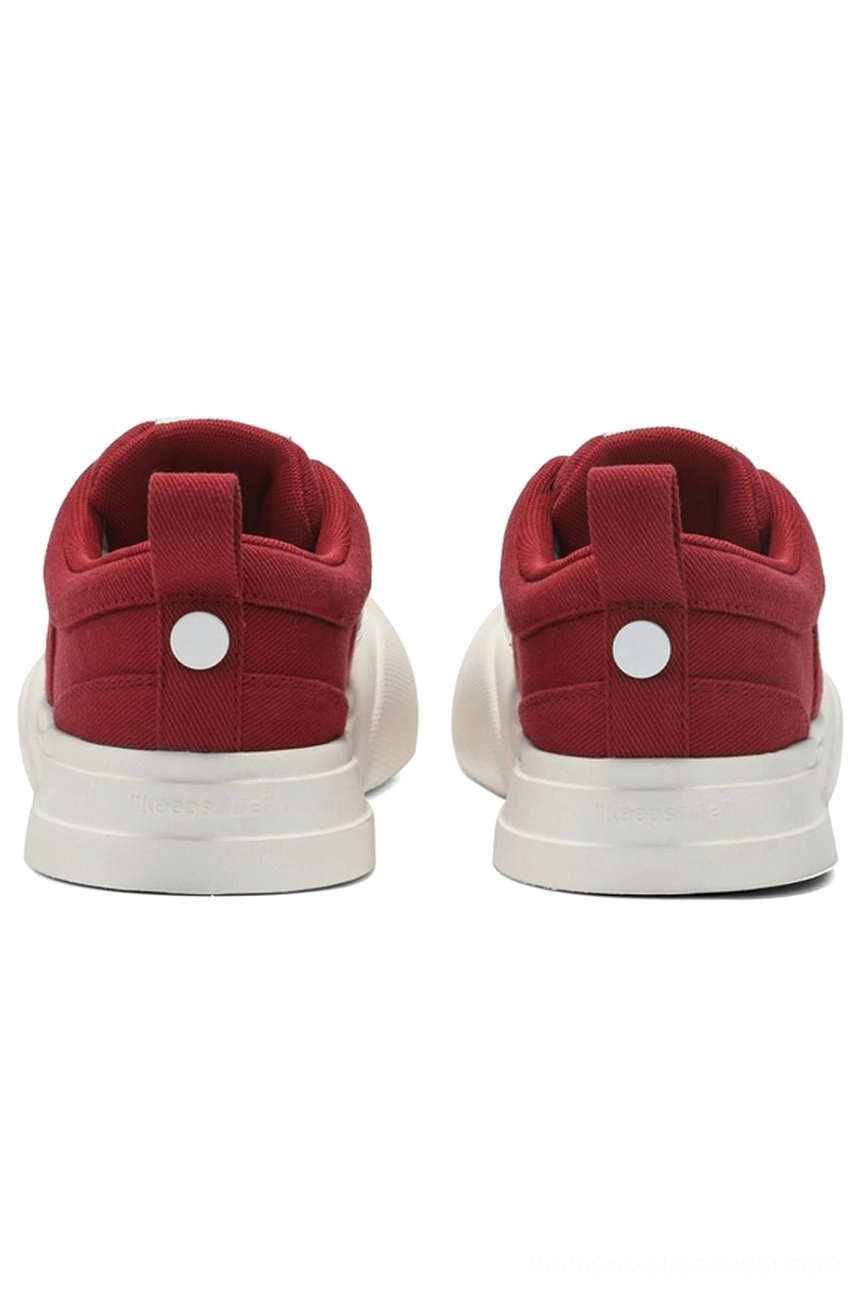 Rear view of red and off-white canvas low-top streetwear sneakers showing the textured rubber outsole, heel pull tabs, and decorative rear button detail