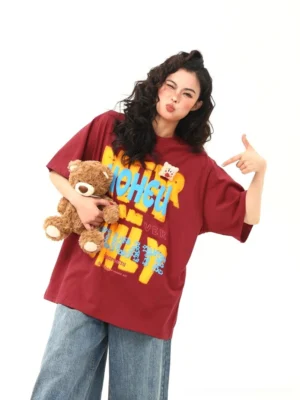 Red oversized graphic streetwear t-shirt with colorful retro text print and teddy bear chest patch front three-quarter view