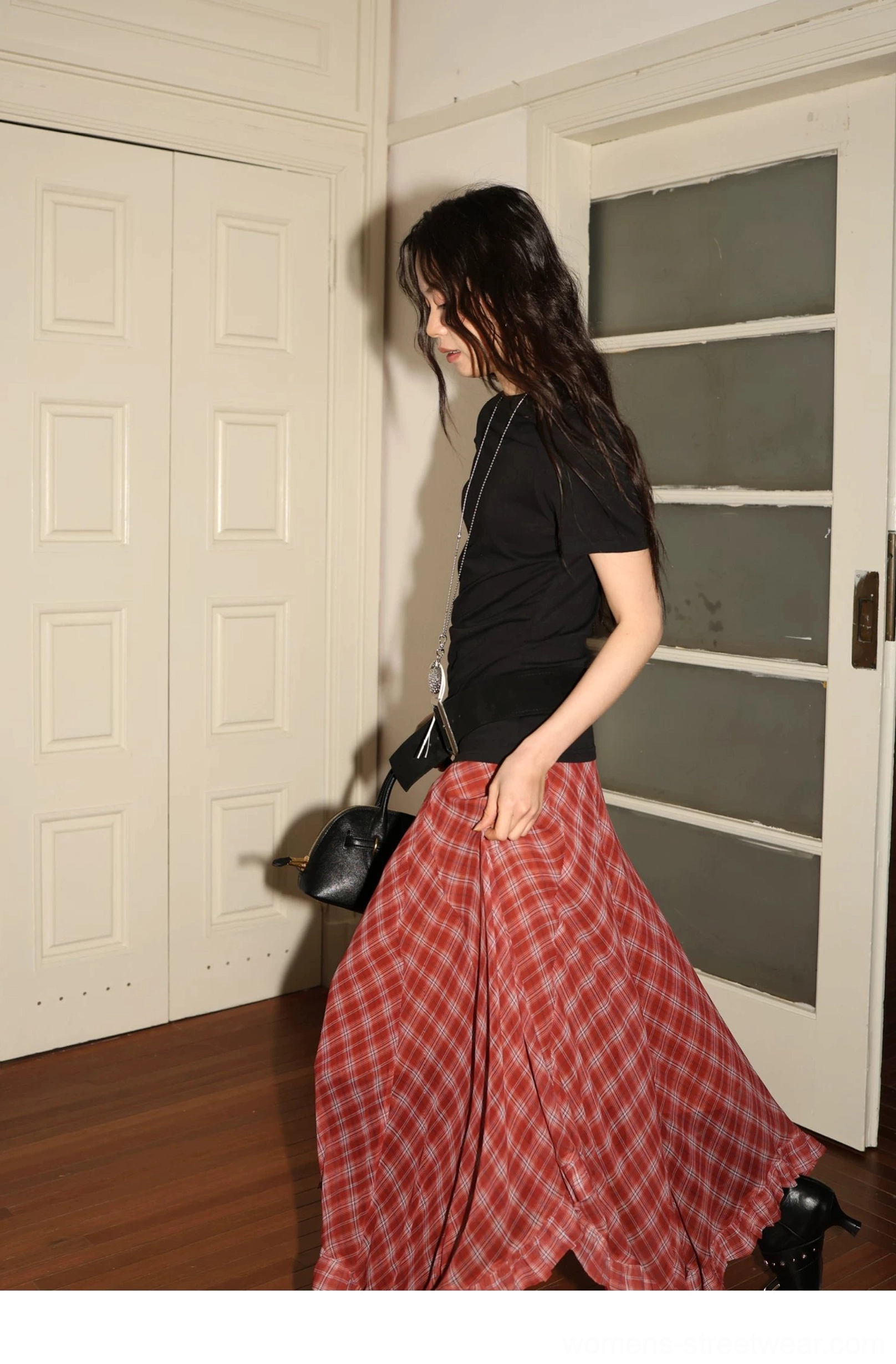Red plaid chiffon asymmetric hem skirt shown in side profile with a black top and crossbody bag