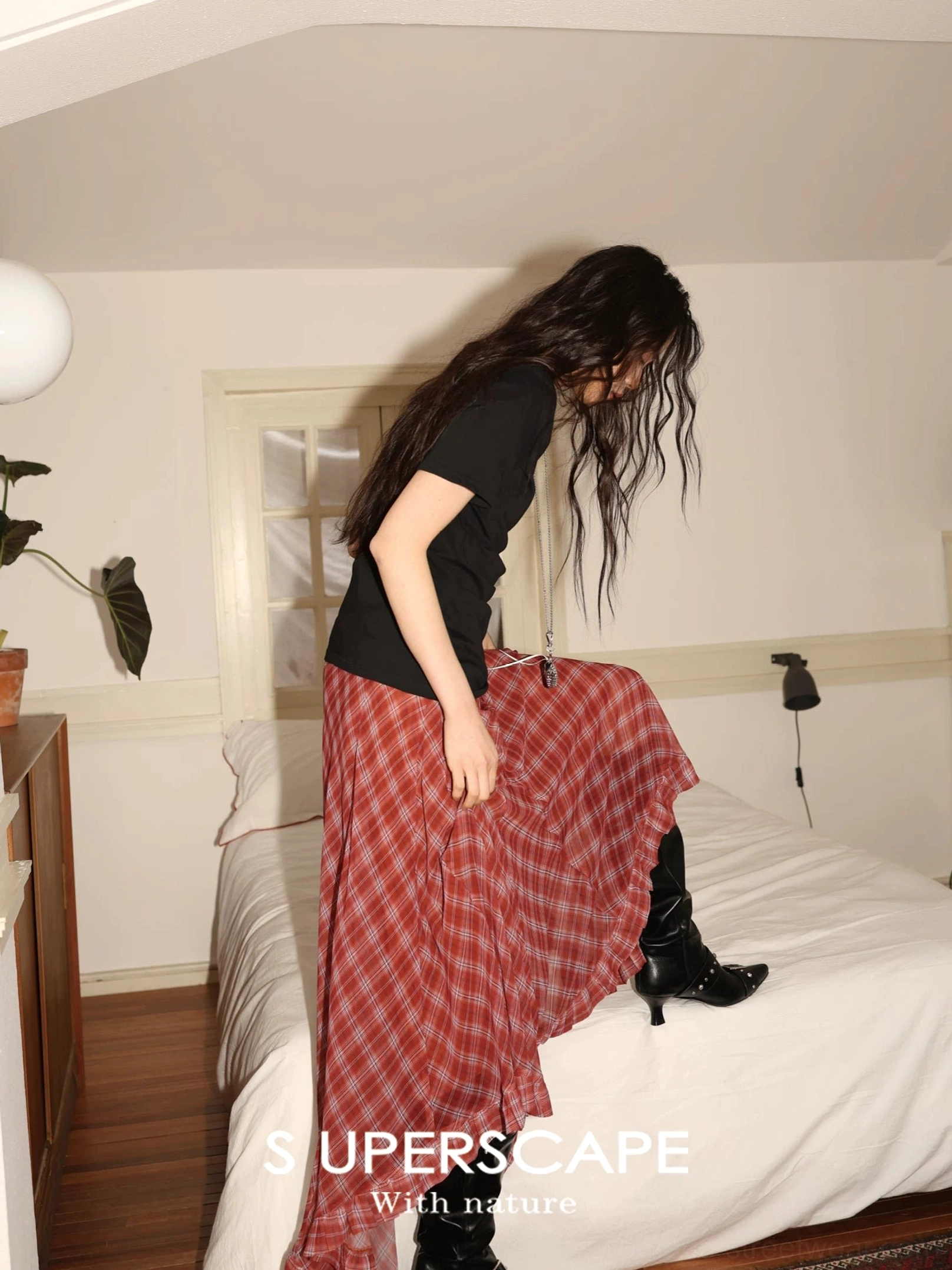 Red plaid chiffon asymmetric maxi skirt styled with a black top and ankle boots in a relaxed bedroom setting