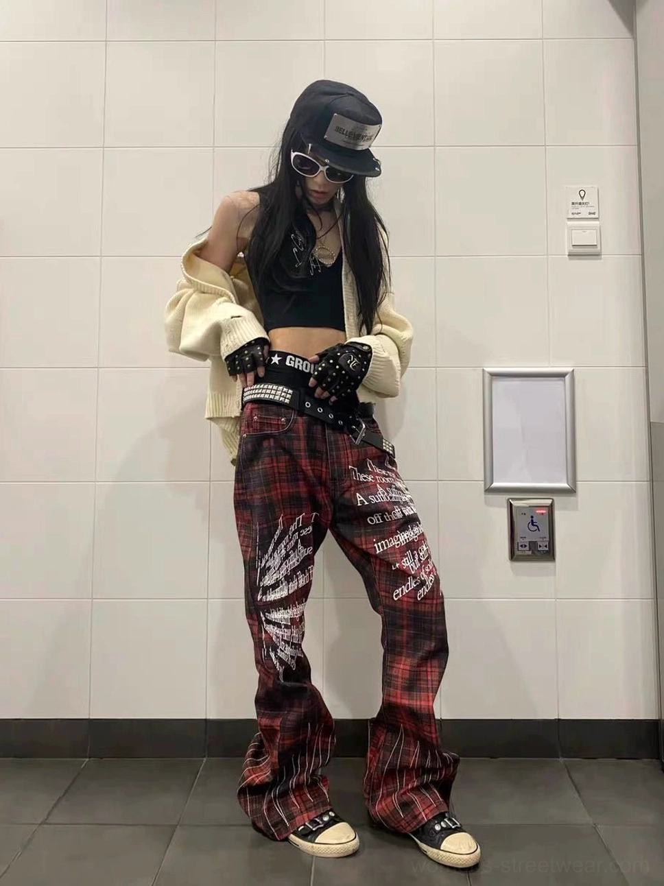 Front view of red plaid Y2K flare pants with white leg graphics styled with a cropped cardigan and platform sneakers