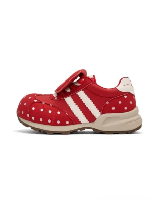 Red polka dot platform sneakers with white side stripes, hook and loop strap, and beige outsole in a three quarter product view