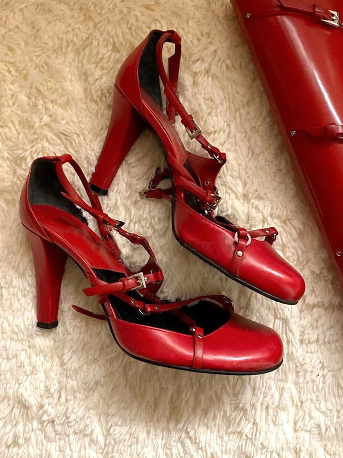 Red round-toe high heel pumps with adjustable crisscross straps, silver metal hardware, and a structured block heel shown from a side angle
