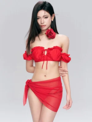 Three-quarter view of bright red ruffled bandeau bikini top, matching swim bottoms, sheer side-tie sarong, and red rose-inspired accessory