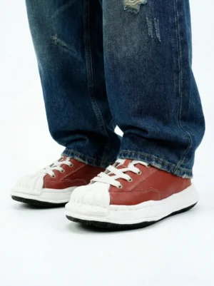 Red shell-toe court sneakers styled with dark blue ripped straight-leg jeans in a casual streetwear outfit