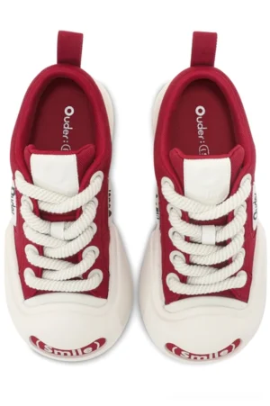 Front overhead view of red canvas low-top sneakers with off-white rubber toe caps, thick contrasting soles, white laces, and playful Smile toe detail