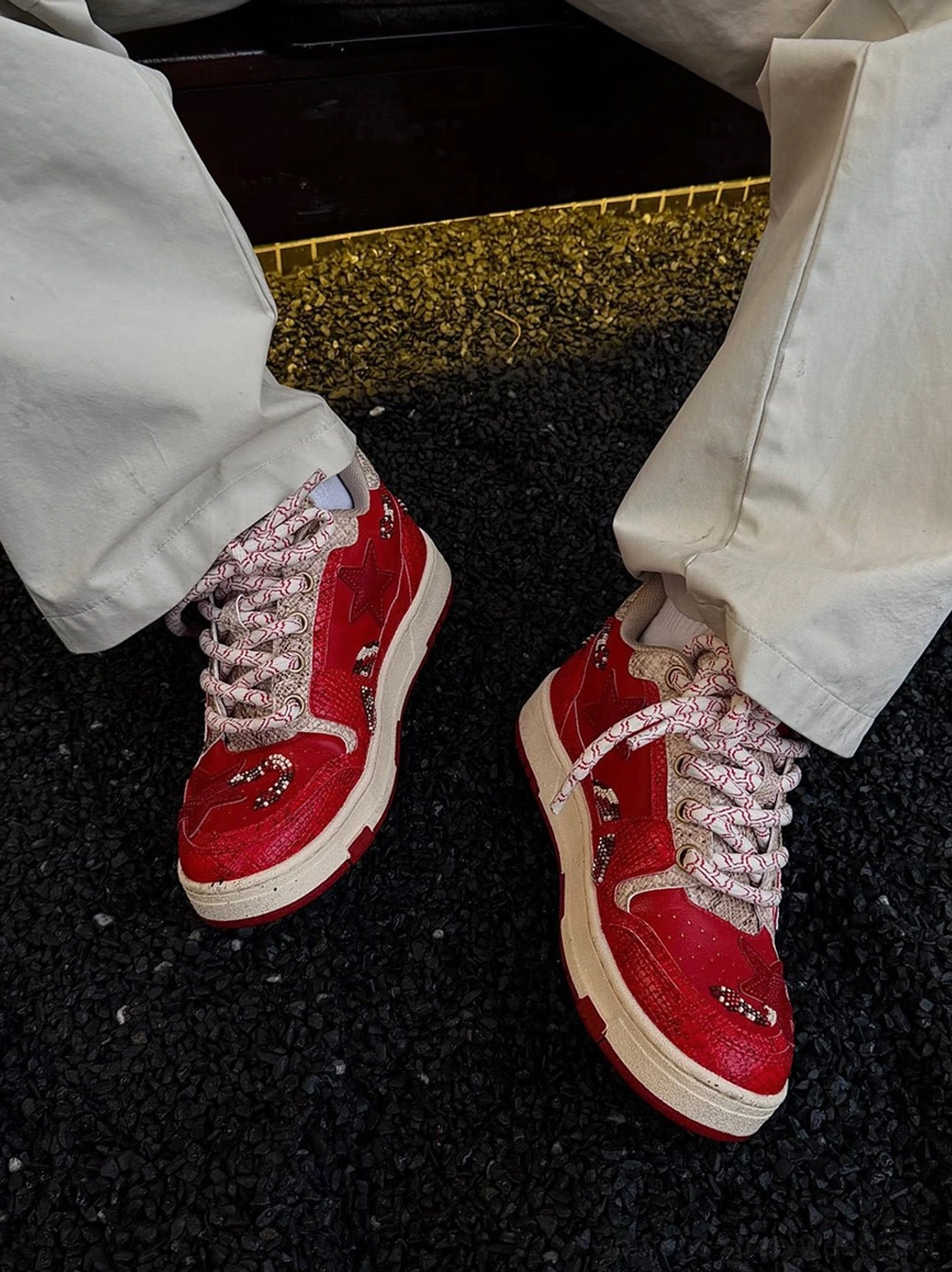 Male model wearing red snake-embossed star court sneakers with relaxed beige trousers in a streetwear outfit