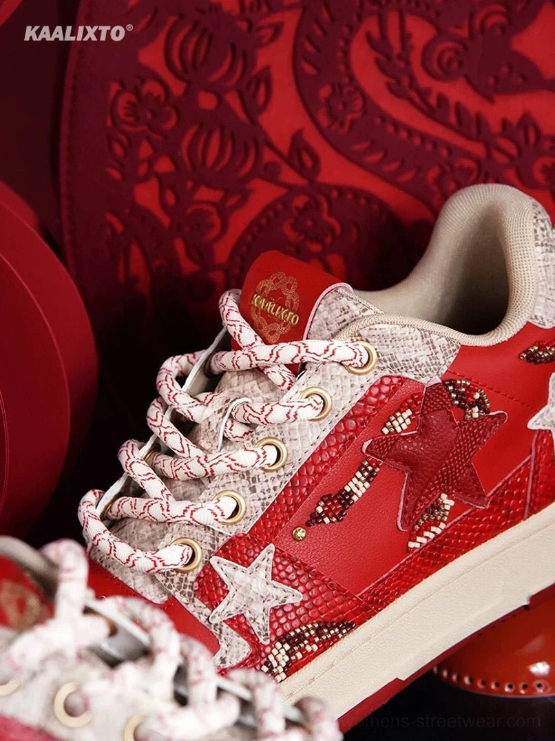Close-up of red snake-patterned sneaker upper with pink-silver rope laces, star details, and tongue logo