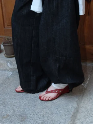Red star-studded thong sandals worn with dark wide-leg jeans and white socks on an outdoor concrete streetwear look