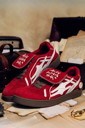 Red suede streetwear court sneakers shown from above on a vintage desk with white graphic logos and gum-colored rubber soles