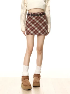 Close front view of a red tartan plaid high-waisted wool skirt styled with a striped top, black leather belt, white socks, and platform boots