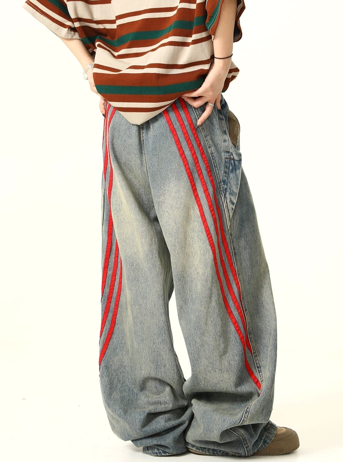 Back angled view of oversized light wash streetwear jeans with diagonal red triple stripes, side pockets, and faded denim texture