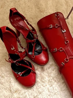 Red vintage-inspired cross-strap round-toe high heels styled beside a matching red handbag on a beige textured carpet