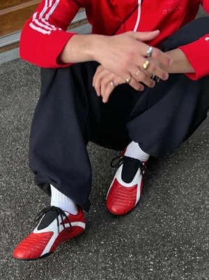 Red and white quilted streetwear sneakers styled with a red track jacket, black sweatpants, and white crew socks on city pavement