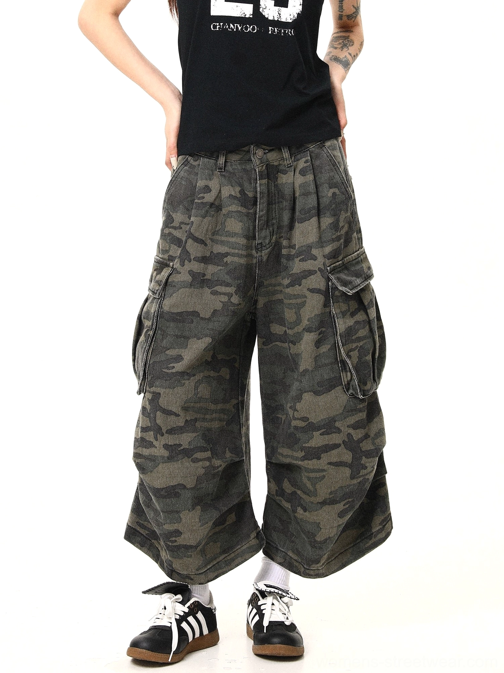 Angled front view of relaxed women’s camouflage cargo pants with multiple utility pockets, loose draping wide legs, pleated high waist, retro sneakers, and modern streetwear styling